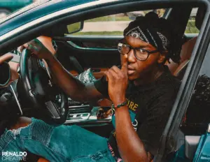 Young Black man in bandana and glasses in car, shushing. Entertainment.