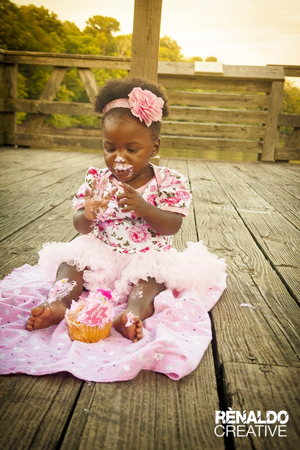 Baby girl in pink dress covered in frosting after eating cupcake