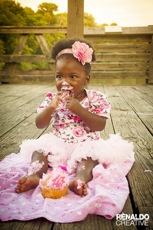 Messy toddler girl in pink tutu eating a birthday cupcake