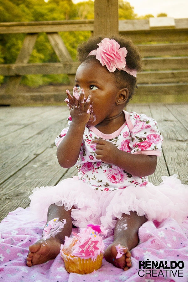 Baby girl covered in frosting eats a pink birthday cupcake